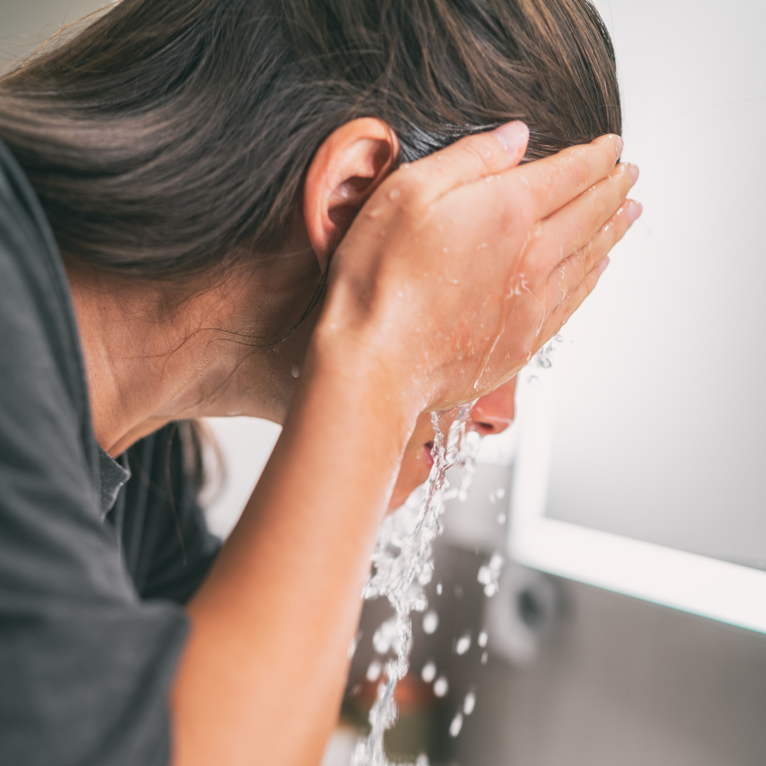 Woman splashing cold water on her face at a sink as part of a nervous system and vagus nerve support routine.