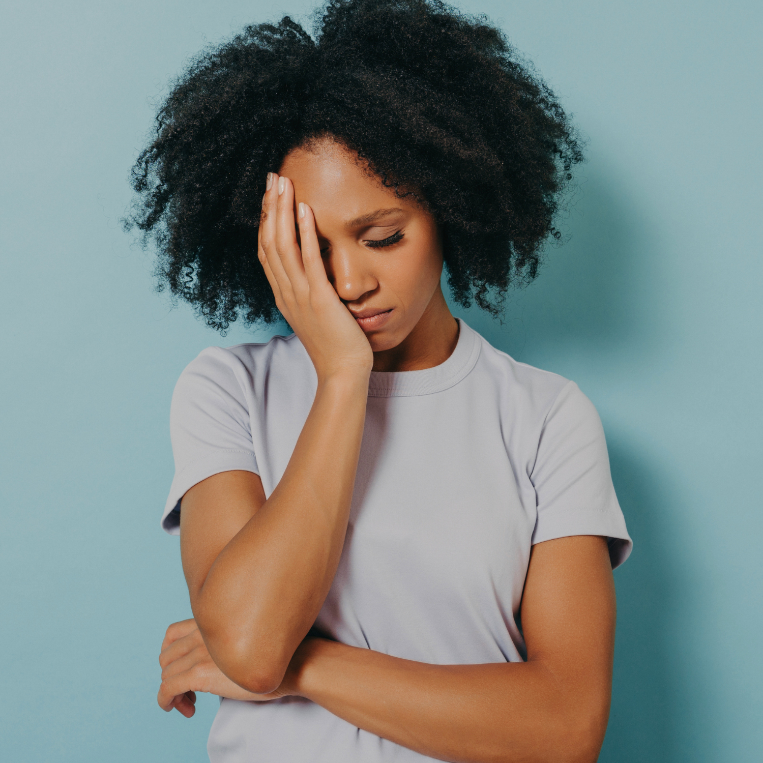 Woman with curly hair holding her head in exhaustion against a teal background, representing chronic stress and its impact on sleep and the nervous system.