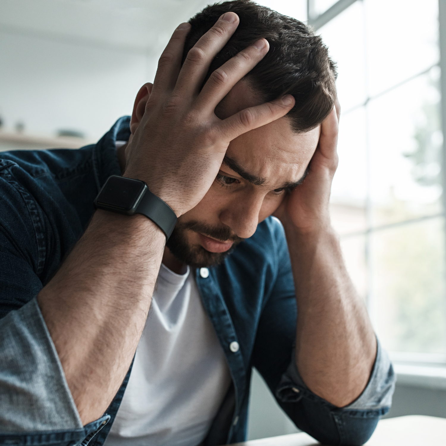 Man sitting with his head in his hands, appearing stressed and overwhelmed, representing morning anxiety and stress.