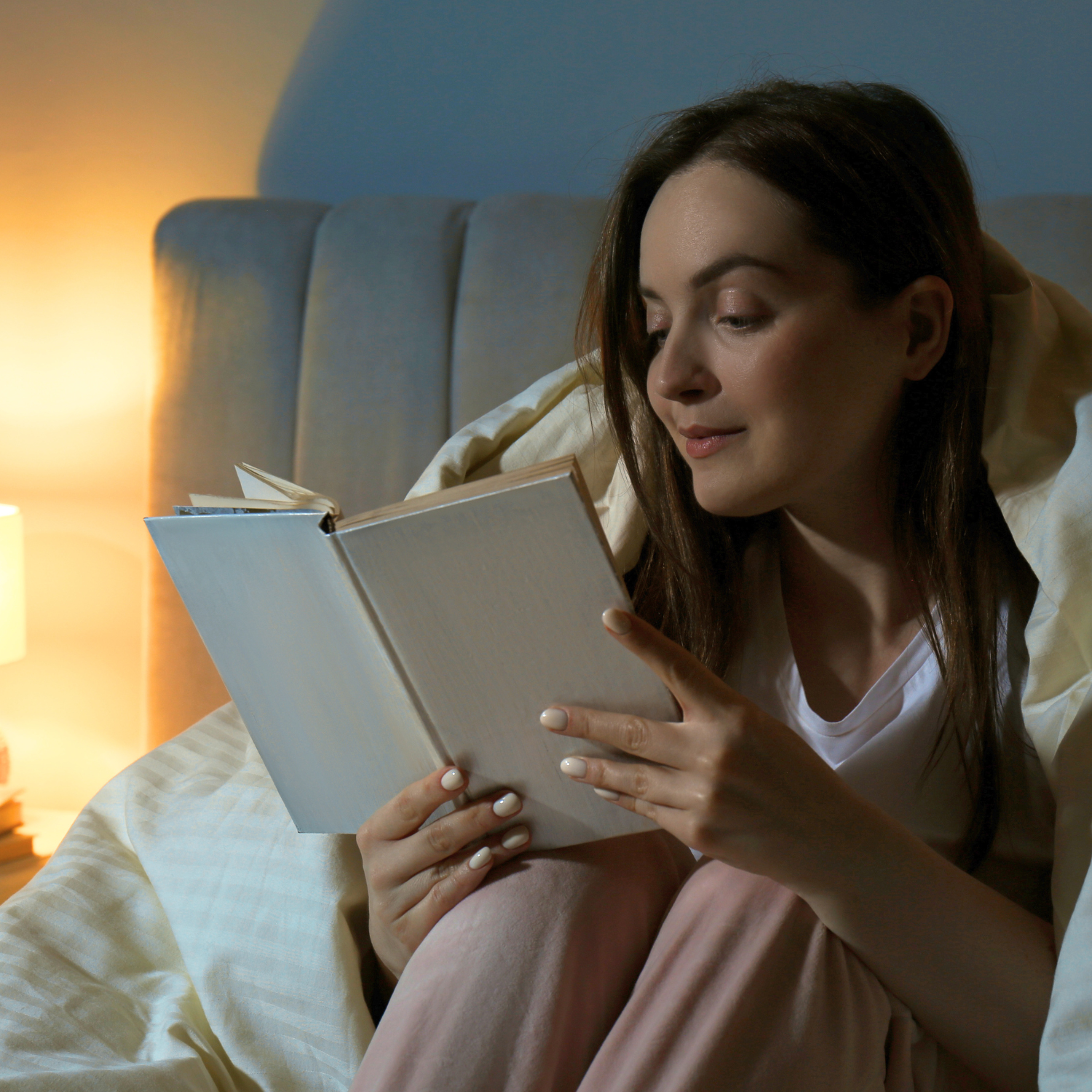 Woman reading a book in bed during a calming nighttime routine for better sleep.