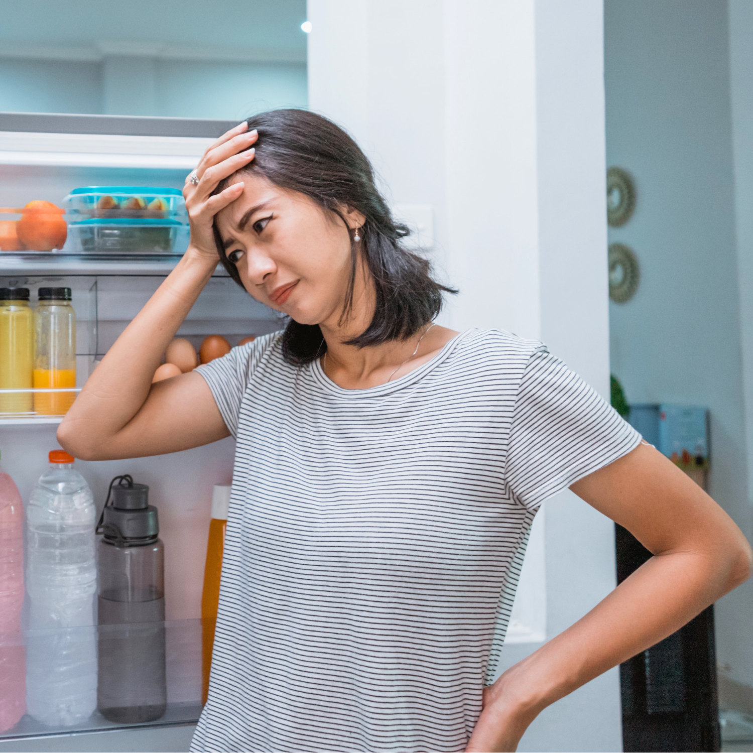 Stressed woman looking in the refrigerator while experiencing food cravings.